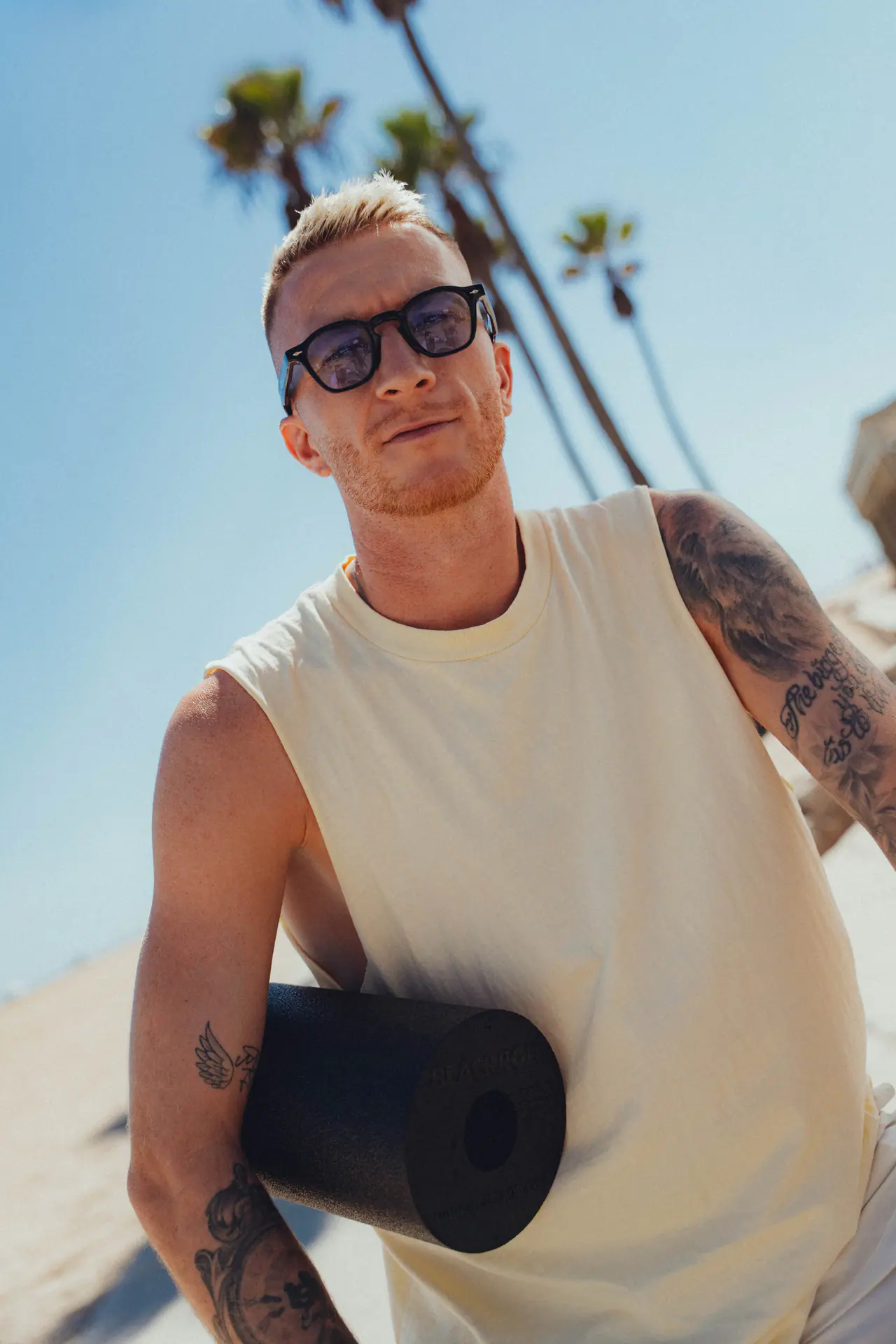 Marco Reus am Strand mit Sonnenbrille, eine Faszienrolle unter dem Arm.
