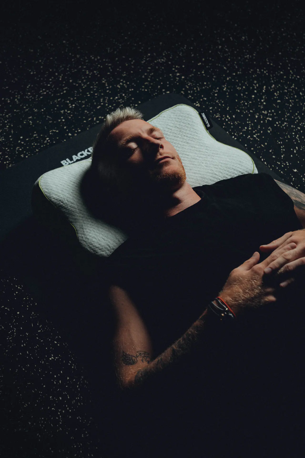 Marco Reus liegt auf einem dunklen Boden, den Kopf auf einem BLACKROLL Recovery Pillow, die Augen geschlossen.