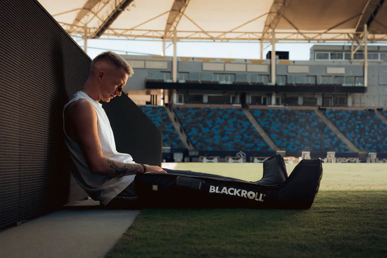 Marco Reus sitzt an der Wand am Rand eines leeren Stadions, die Beine in BLACKROLL Compression Boots.
