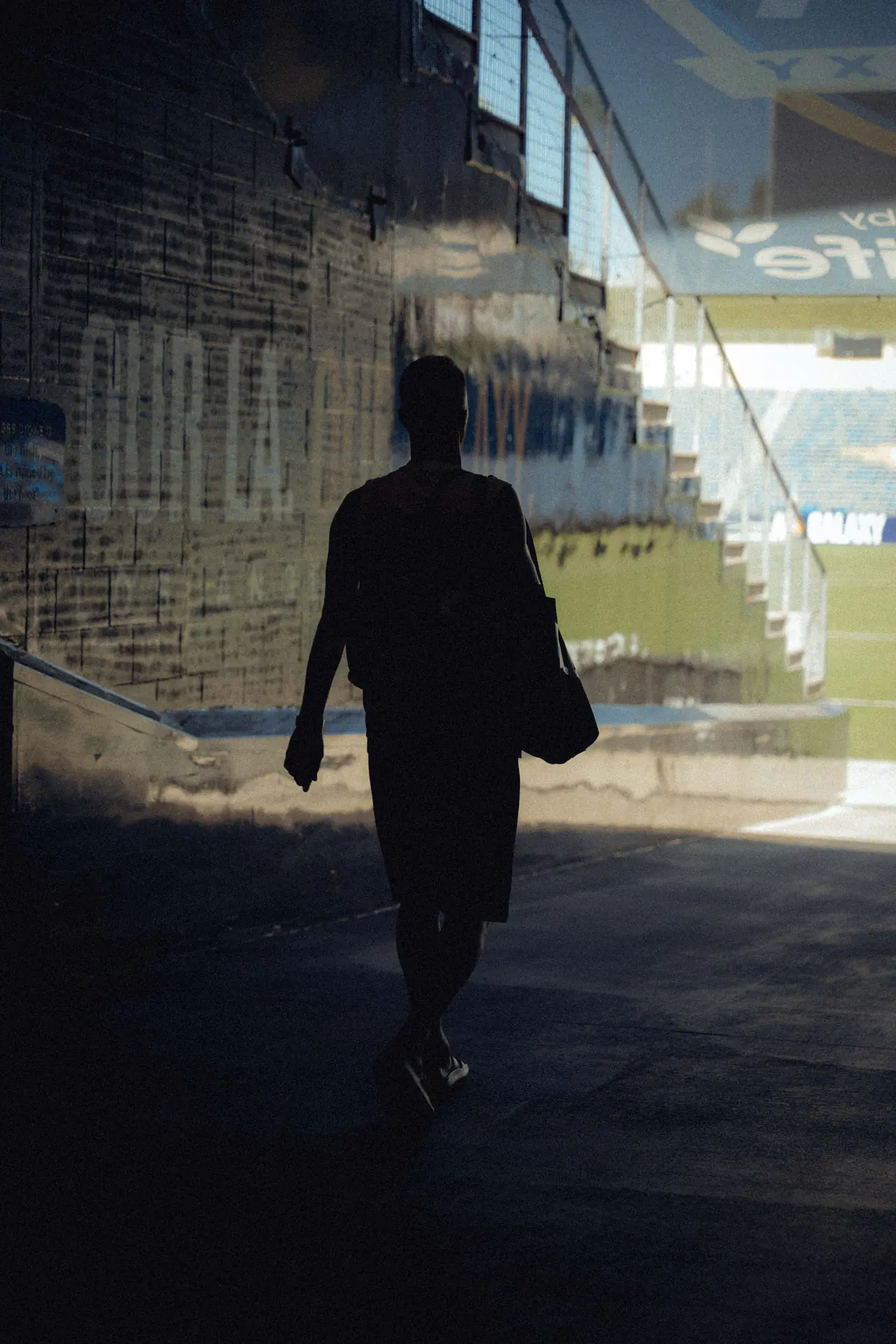 Marco Reus geht, von hinten gesehen, durch den schattigen Spielertunnel auf das sonnige Stadion zu, eine Tasche über der Schulter.